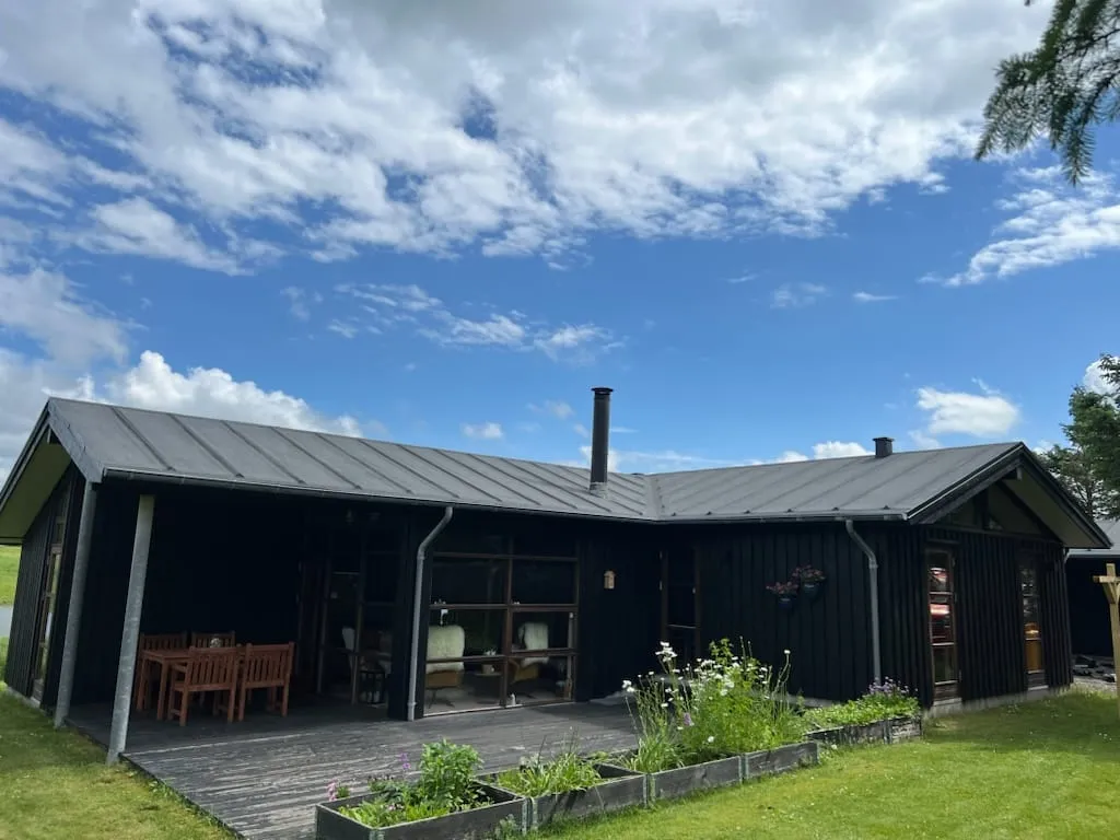 Billedet viser et moderne sort træhus med skråt tag og en overdækket terrasse.